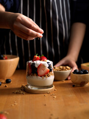 Female adding granola on a glass of granola with Greek yogurt and fresh berries