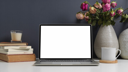 Close up view of worktable with laptop, books, cup and flower vase in home office