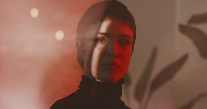 Portrait of young serious woman looking at camera with red light and smoke machine 
