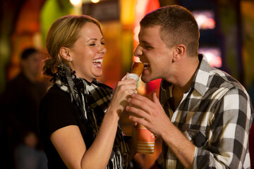 Young woman feeding her boyfriend a corn dog at an amusement park