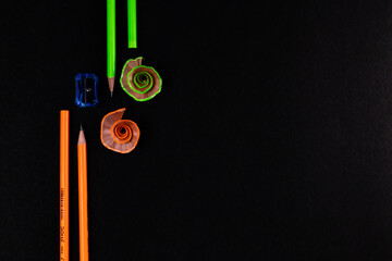 Four green and orange pencils with a blue sharpener on black background.