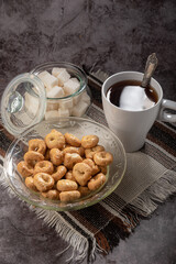 Tea in white lace with a handle, a spoon, on a napkin with a sugar bowl with a lump of sugar and tarallini in a glass plate on a gray background