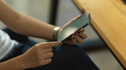 Female hands holding smartphone while sitting at workplace