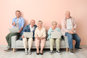 Senior people with different devices sitting on sofa in room