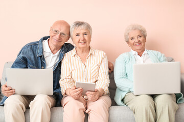 Senior people with different devices sitting on sofa in room