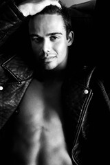 Semi naked handsome man sitting in leather armchair with open shirt revealing sixpack abs and open jeans