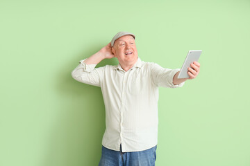 Senior man using tablet computer on color background