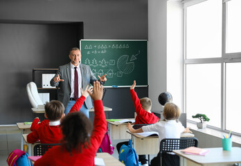 Male teacher and cute children with raised hands during lesson in classroom