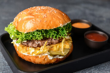 Tray with tasty burger and sauces on dark background