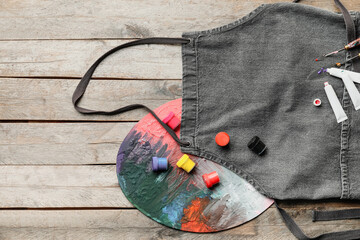 Apron and set of artist's supplies on wooden background