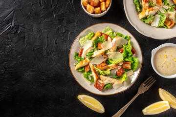 Caesar salad with chicken and Parmesan, overhead flat lay shot on a black background with copy space