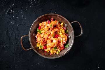 Spicy shrimps with corn in a copper pan, shot from the top on a black background
