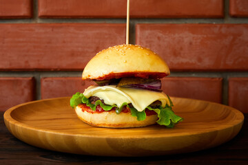 Burger with beef, cheese and lettuce leaves on a wooden plate on a brick wall background. Close-up, selective focus
