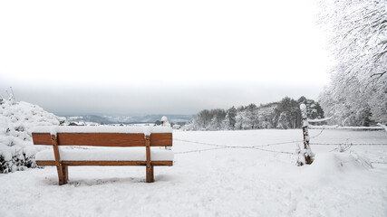 Verschneite Holzbank, im Hintergrund die weißen Ausläufer der Eifel