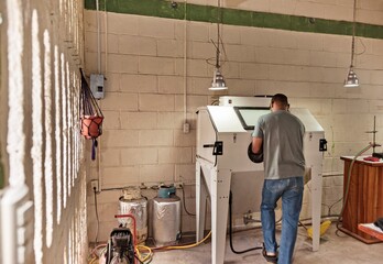 Ecuador, Galapagos Islands, Man sandblasting glass to make souvenir glasses out of bottles in artisan workshop