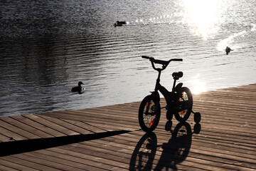 Silhouette of a children bicycle on the lake shore on swimming ducks background. Spring leisure in...