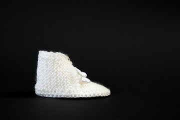 Handmade knitted white shoes for small children. Adorable newborn baby shoes isolated on black background.