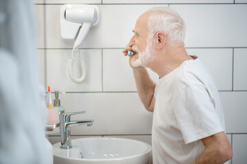Gray-haired man in white tshirt cleaning his teeth