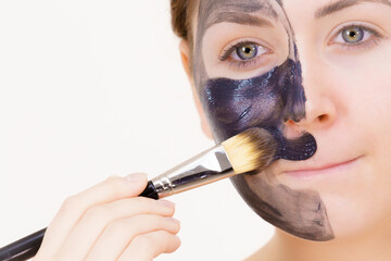 Female applying black mud facial mask