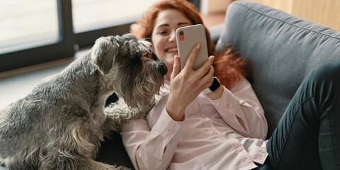 Girl resting while sitting with her dog on the couch and using smartphone