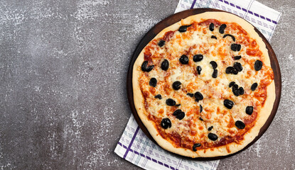 Rustic pizza with mozzarella and olives on a round wooden cutting board on a dark background. Top view, flat lay
