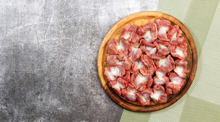 Raw chicken gizzards on a round wooden cutting board on a dark grey background. Top view, flat lay