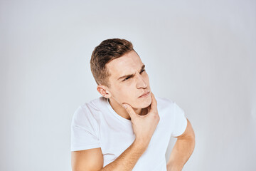 Emotional man in a white t-shirt holds his hand on his face light background