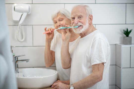 Elderly couple brushing their teeth together and looking contented