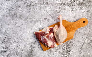 Raw duck drumsticks and thighs on a small cutting wooden board on a dark grey background. Top view, flat lay
