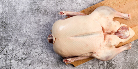 Whole raw duck on a rectangular cutting wooden board on a dark grey background. Top view, flat lay