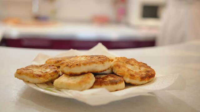 On the table, on a white plate, with a white waffle napkin, there are crispy rounded cutlets; in the background, a woman in a white terry robe who cooked them is walking in blur.