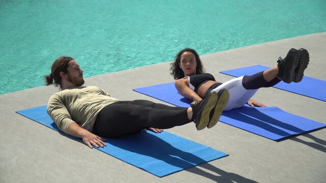 young fitness couple doing exercise sit ups strengthen stomach and  back muscle together on yoga mat  by pool in sport club . fit woman and trainer man training workout outdoors