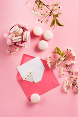 Rose macaroons in gift box, Cherry blossoms, empty envelope. Sweet macarons present on pink background.