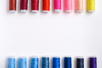 Multi-colored spools of thread arranged evenly along the edges on a white background. There is an...