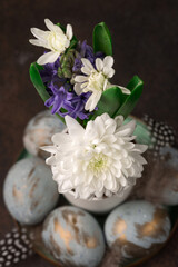  Easter Decoration with gray golden eggs, quail feathers, hyacinth daisy flowers on dark wooden background.
