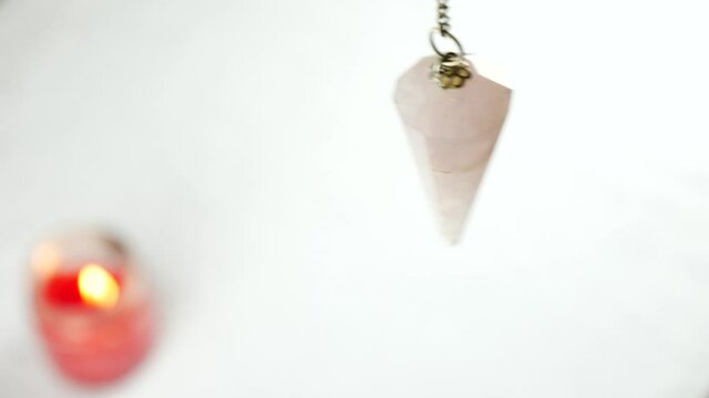 Close-up of a pendulum moving on a white background. Red blurred candle on the left.