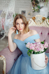 Close-up portrait of a beautiful blonde woman. She's wearing a blue, airy dress. In her hands is a box of flowers