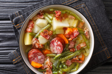 Luxembourgish soup of green beans, potatoes, leeks, carrots with the addition of sausages and bacon close-up in a plate on the table. Horizontal top view from above