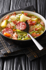 Bouneschlupp is a traditional Luxemburgish green bean soup with potatoes, bacon, and onions close-up in a plate on the table. Vertical