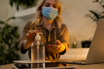 Protect yourself during a pandemic, epidemic. Young woman in office spraying a disinfector on her hands, a medical mask on her