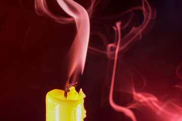 Closeup of an extinguished yellow candle with smoke on a maroon background