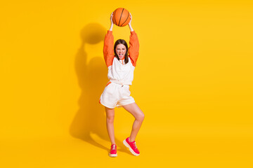 Fototapeta na wymiar Full length photo portrait of celebrating woman holding basketball over head isolated on vivid yellow colored background