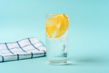 A glass of water with ice and lemon on a light blue background, the concept of a healthy lifestyle