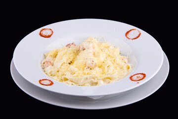 Fettuccine with salmon in cream sauce on white plate on black background