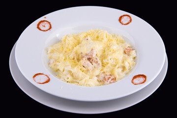 Fettuccine with salmon in cream sauce on white plate on black background
