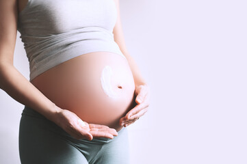 Pregnant woman applying moisturizer cream on her belly. Body skin care during pregnancy.