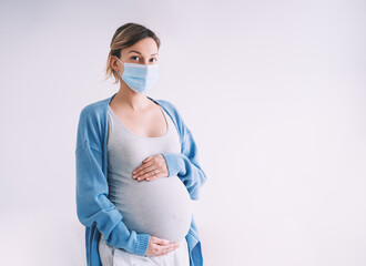 Young pregnant woman in medical mask hugging belly. Pregnancy and childbirth during infectious...