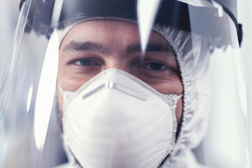 Fototapeta na wymiar Medic with visor and ppe protection equipment looking at camera in laboratory. Overworked researcher dressed in protective suit against invection with coronavirus during global epidemic.