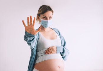 Pregnancy and childbirth during Infections. Pregnant woman in medical mask hugging belly showing STOP gesture. Protection and prevention during viruses, mother care of her and unborn baby health.