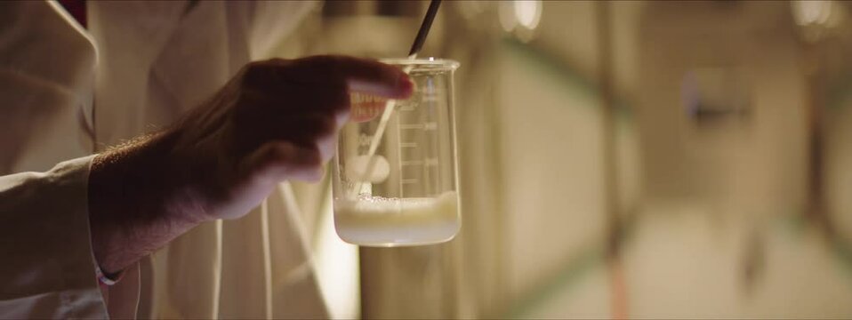 Food scientist pouring beer into a beaker. Beer foam in a beaker. Scientist taking beer sample for analysis. Brewery, factory concept.